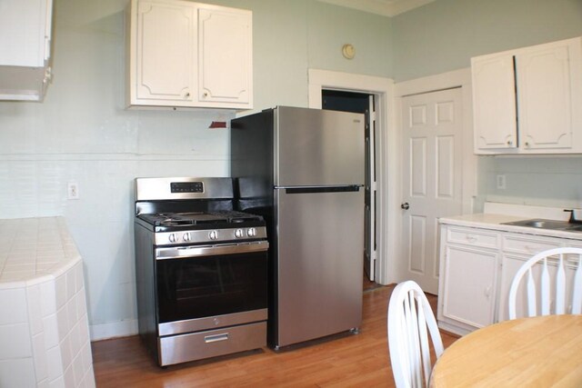 1611 Chapman St, Houston, TX 77009 - kitchen featuring appliances with stainless steel finishes, white cabinets, light wood-type flooring, and a sink