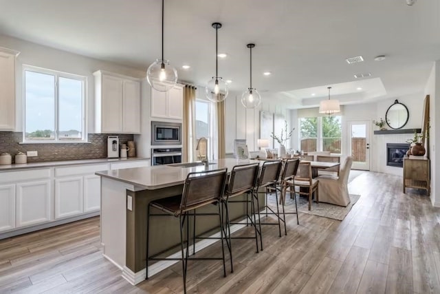 5238 Oakland Bluff Ln, Richmond, TX 77469 - kitchen featuring stainless steel appliances, a tray ceiling, a sink, light wood-type flooring, and a center island with sink