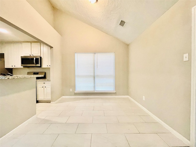 16303 Napa Vine Dr, Houston, TX 77053 - kitchen with stainless steel microwave, lofted ceiling, baseboards, white cabinetry, and light stone counters