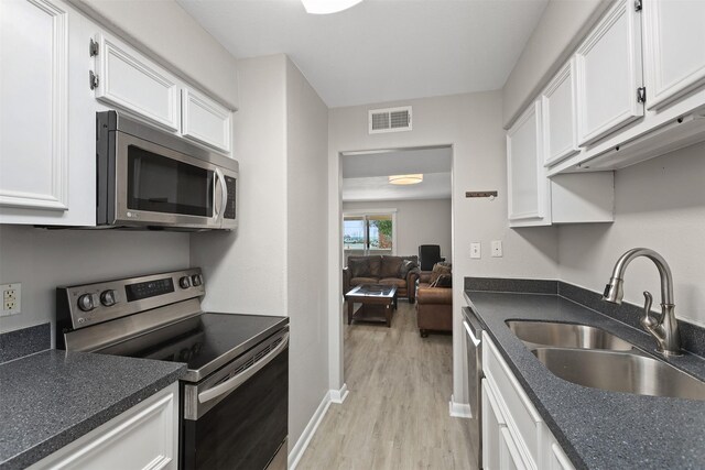 215 Post Office St Unit 1208, Galveston, TX 77550 - kitchen featuring appliances with stainless steel finishes, a sink, light wood-style flooring, and white cabinets