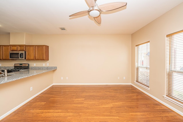 2212 Naomi St, Houston, TX 77054 - kitchen featuring stainless steel microwave, gas range, brown cabinetry, light wood-type flooring, and ceiling fan
