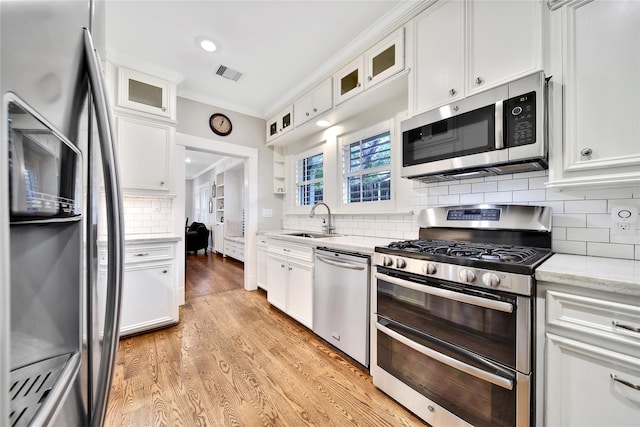 423 Pecore St, Houston, TX 77009 - kitchen with stainless steel appliances, white cabinets, light wood finished floors, crown molding, and tasteful backsplash
