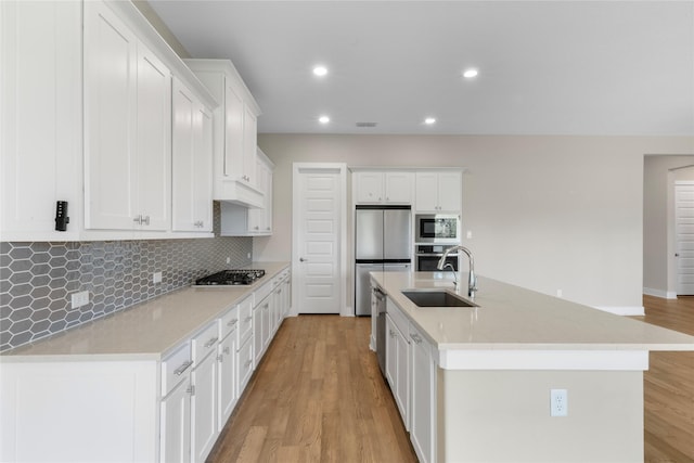 24815 Pavonia Lake Ln, Tomball, TX 77375 - kitchen featuring stainless steel appliances, white cabinets, tasteful backsplash, light wood-style flooring, and a center island with sink