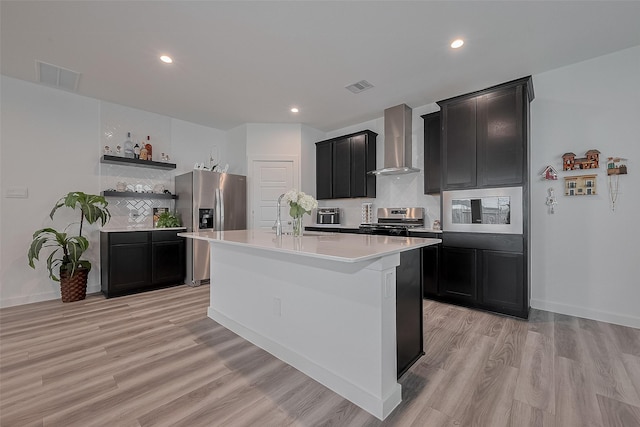 12319 Brandenburg Gate Dr, Houston, TX 77047 - kitchen featuring wall chimney range hood, appliances with stainless steel finishes, dark cabinetry, decorative backsplash, and light wood finished floors