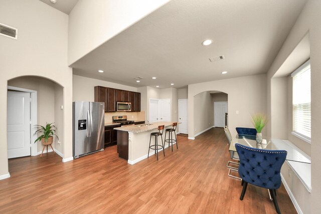 24739 Lorenzo Glaze Trl, Katy, TX 77493 - kitchen with appliances with stainless steel finishes, arched walkways, a center island with sink, light wood finished floors, and dark brown cabinets