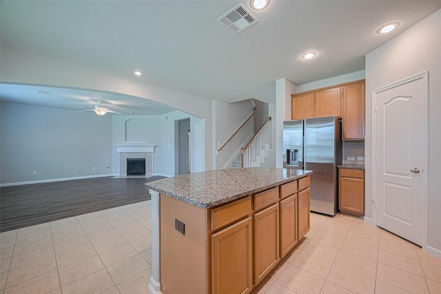 24523 Carlton Springs Ln, Katy, TX 77494 - kitchen featuring stainless steel fridge with ice dispenser, a ceiling fan, light tile patterned floors, a fireplace with flush hearth, and a center island
