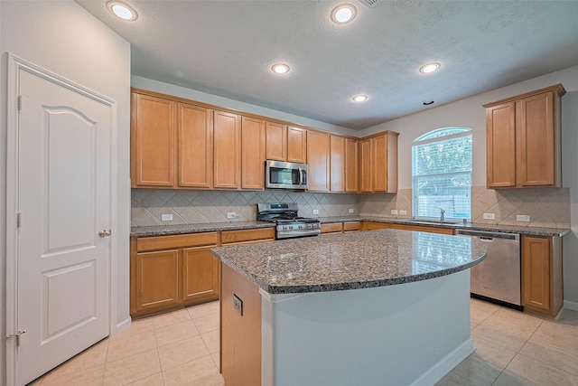 24523 Carlton Springs Ln, Katy, TX 77494 - kitchen with appliances with stainless steel finishes, light tile patterned floors, dark stone counters, a sink, and a center island