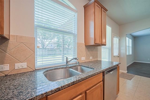 24523 Carlton Springs Ln, Katy, TX 77494 - kitchen featuring stainless steel dishwasher, a sink, light tile patterned floors, tasteful backsplash, and dark stone counters