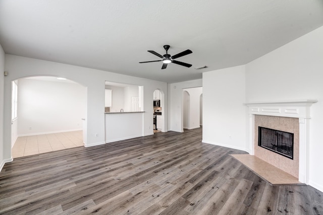 16906 Shoal Park Dr, Cypress, TX 77429 - unfurnished living room featuring arched walkways, a ceiling fan, a tiled fireplace, wood finished floors, and baseboards