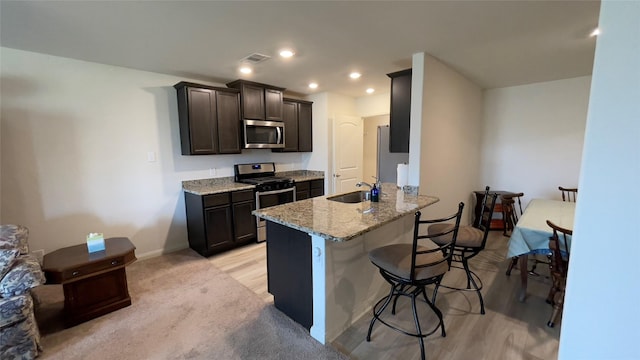 21138 Titian Dr, Magnolia, TX 77355 - kitchen with appliances with stainless steel finishes, a breakfast bar area, light stone countertops, dark brown cabinetry, and a peninsula