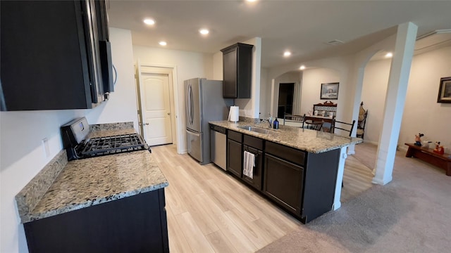 21138 Titian Dr, Magnolia, TX 77355 - kitchen with stainless steel appliances, arched walkways, a peninsula, a sink, and light stone countertops