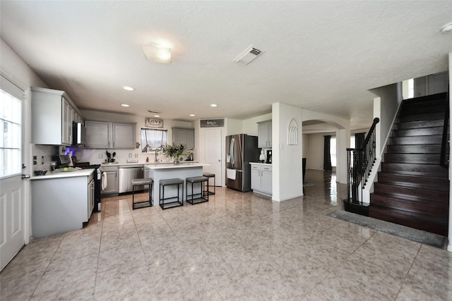 9107 S Ferndale Place Dr, Houston, TX 77064 - kitchen featuring stainless steel appliances, a breakfast bar area, arched walkways, a kitchen island, and gray cabinetry