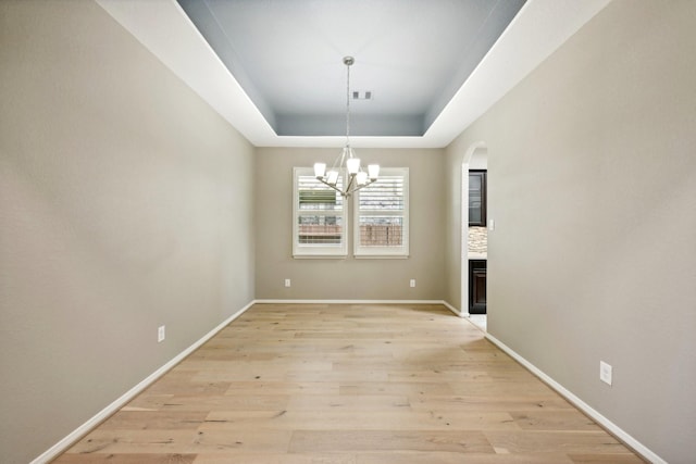10315 Silver Shield Way, Tomball, TX 77375 - unfurnished dining area featuring a raised ceiling, light wood-type flooring, a chandelier, arched walkways, and baseboards