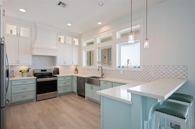 852 W Lazy Ln, Crystal Beach, TX 77650 - kitchen with stainless steel appliances, a peninsula, white cabinets, tasteful backsplash, and light wood-type flooring
