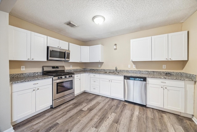 4446 Castor St, Houston, TX 77022 - kitchen with appliances with stainless steel finishes, light wood-style flooring, a sink, white cabinetry, and a textured ceiling