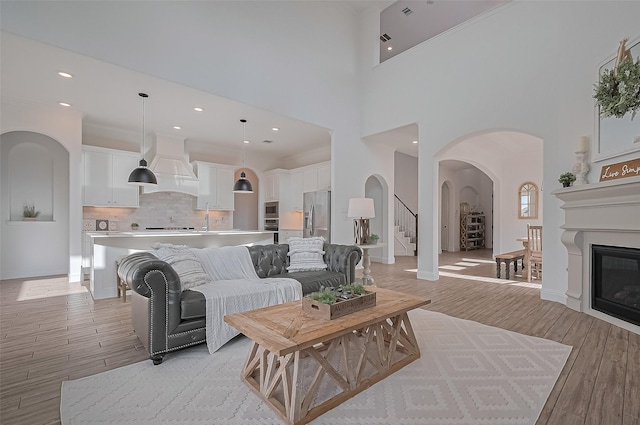 18003 Winding Willow Oak Way, Cypress, TX 77433 - living area with light wood-type flooring, a high ceiling, a glass covered fireplace, arched walkways, and stairway