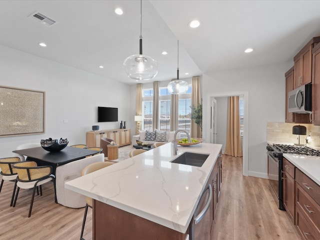 9221 Washington Hts, Houston, TX 77063 - kitchen featuring appliances with stainless steel finishes, a sink, light wood-style flooring, backsplash, and a center island with sink