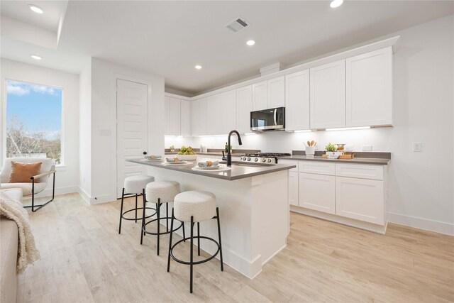 5322 Rue St, Houston, TX 77033 - kitchen featuring stainless steel microwave, light wood-style flooring, a breakfast bar area, recessed lighting, and an island with sink