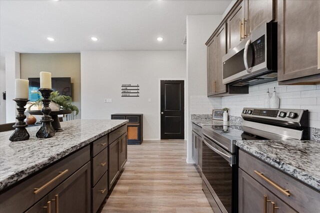 16997 White Birch Ln, Conroe, TX 77385 - kitchen with stainless steel appliances, light wood-style flooring, light stone counters, tasteful backsplash, and dark brown cabinetry