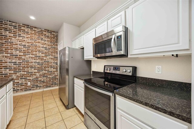 2255 Braeswood Park Dr Unit 105, Houston, TX 77030 - kitchen featuring stainless steel appliances, brick wall, white cabinets, light tile patterned flooring, and dark stone countertops