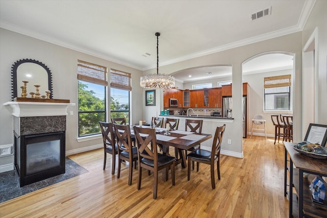 1814 Rosalie St, Houston, TX 77004 - dining room featuring light wood-type flooring, a premium fireplace, a chandelier, ornamental molding, and arched walkways