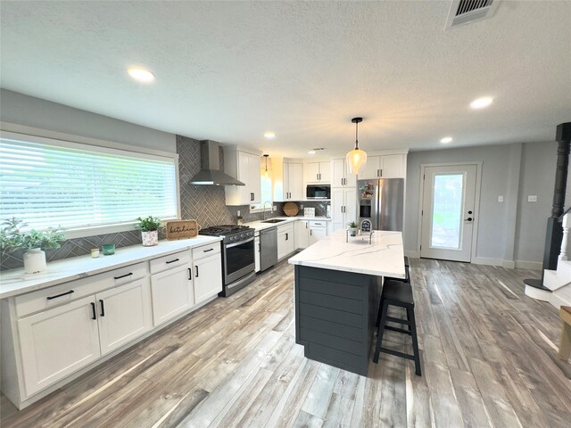 5301 Hemlock Dr, Baytown, TX 77521 - kitchen with stainless steel appliances, wall chimney range hood, a sink, light wood-type flooring, and white cabinets