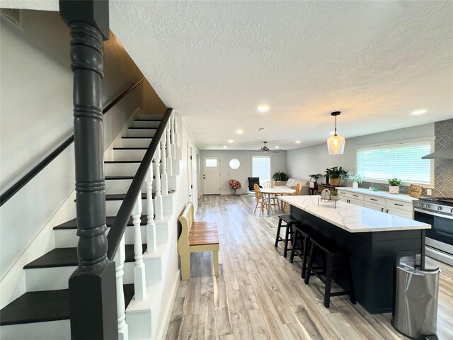5301 Hemlock Dr, Baytown, TX 77521 - kitchen featuring stainless steel range with gas stovetop, a textured ceiling, a kitchen breakfast bar, a ceiling fan, and light wood-style flooring