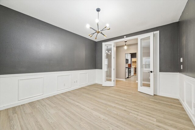 28519 Peper Hollow Ln, Spring, TX 77386 - empty room with french doors, a chandelier, wainscoting, light wood-style floors, and a decorative wall