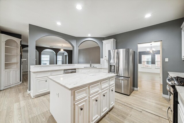28519 Peper Hollow Ln, Spring, TX 77386 - kitchen featuring appliances with stainless steel finishes, a sink, light wood finished floors, light stone counters, and arched walkways