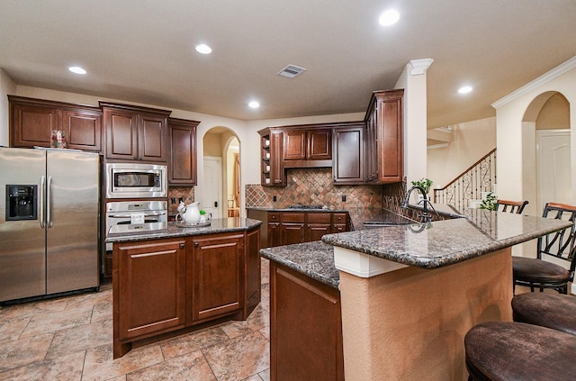 28030 Sugarside Glen Dr, Katy, TX 77494 - kitchen featuring appliances with stainless steel finishes, a sink, arched walkways, a peninsula, and backsplash