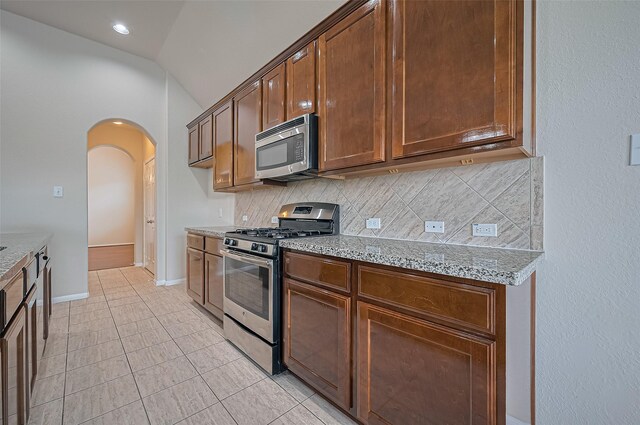 3934 Medici Ct, Missouri City, TX 77459 - kitchen featuring appliances with stainless steel finishes, decorative backsplash, arched walkways, light stone counters, and lofted ceiling