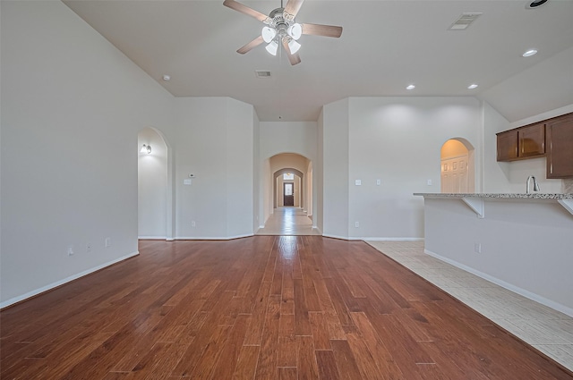 3934 Medici Ct, Missouri City, TX 77459 - unfurnished living room with arched walkways, a ceiling fan, light wood-style flooring, vaulted ceiling, and a sink