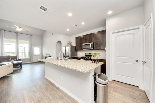 24810 Puccini Pl, Katy, TX 77493 - kitchen featuring appliances with stainless steel finishes, a sink, light wood-type flooring, dark brown cabinets, and an island with sink