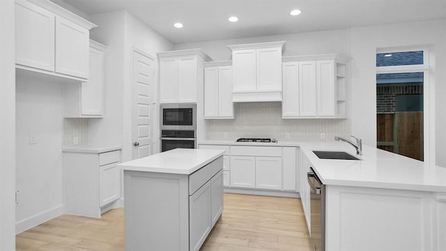 7439 Denali Dr, Katy, TX 77493 - kitchen featuring stainless steel appliances, a sink, light wood-style flooring, a peninsula, and tasteful backsplash