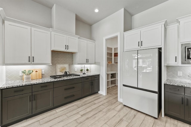 4215 Wooded Isle Way, Fulshear, TX 77441 - kitchen with appliances with stainless steel finishes, white cabinetry, decorative backsplash, light wood-style flooring, and light stone counters