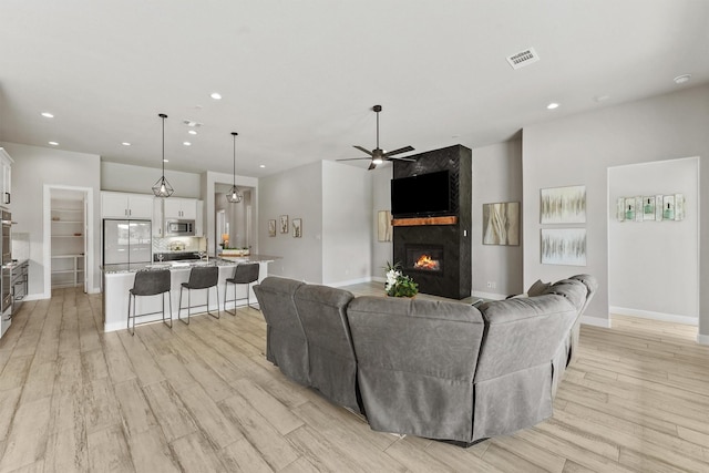 4215 Wooded Isle Way, Fulshear, TX 77441 - living room with ceiling fan, a large fireplace, light wood-style floors, baseboards, and recessed lighting