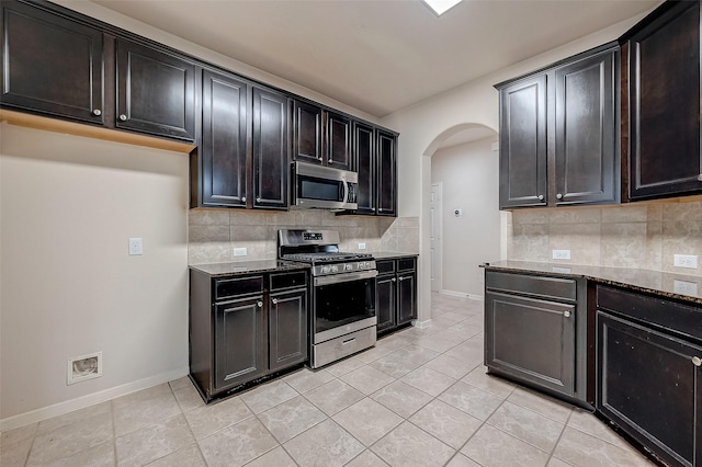 13322 Mesquite Stone Ln, Richmond, TX 77407 - kitchen with stainless steel appliances, arched walkways, baseboards, and dark stone counters