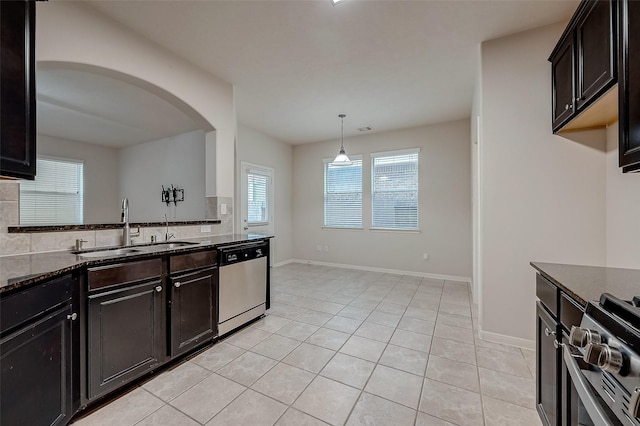 13322 Mesquite Stone Ln, Richmond, TX 77407 - kitchen with stainless steel appliances, a sink, dark stone counters, arched walkways, and light tile patterned flooring