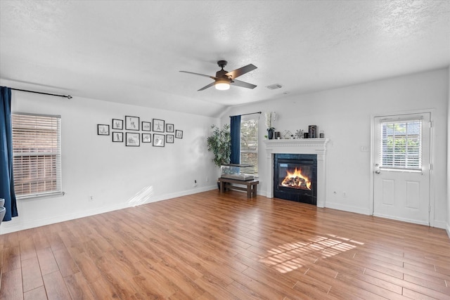 11411 Sugarbush Ridge Ln, Houston, TX 77089 - unfurnished living room featuring light wood-style floors, ceiling fan, a glass covered fireplace, healthy amount of natural light, and a textured ceiling