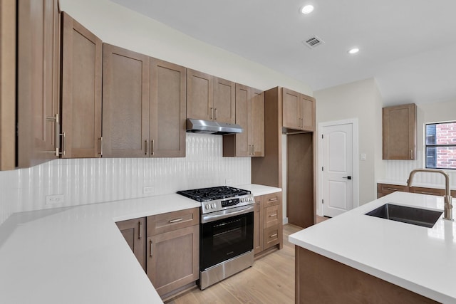 23135 Tranquil Springs Ln, Katy, TX 77494 - kitchen with stainless steel gas stove, a sink, under cabinet range hood, light wood finished floors, and decorative backsplash
