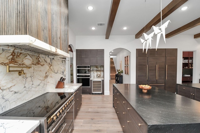 7153 Fm 1458th Rd, Sealy, TX 77474 - kitchen with stainless steel electric range, arched walkways, wall chimney exhaust hood, wine cooler, and beam ceiling