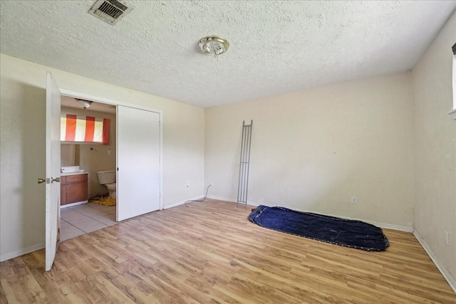 2630 35th St, Pinehurst, TX 77630 - unfurnished bedroom featuring light wood finished floors, a textured ceiling, baseboards, and ensuite bathroom