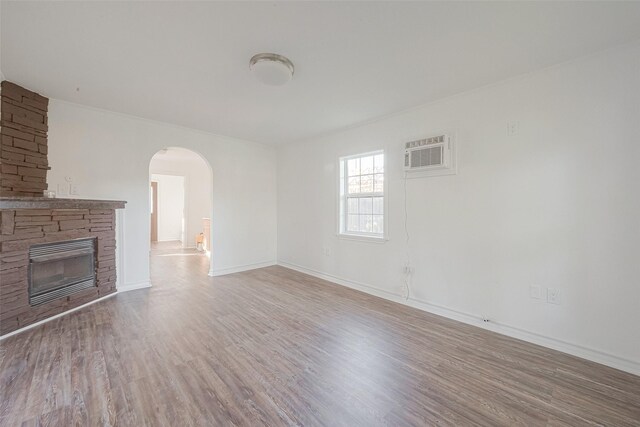 607 Speed St, Wharton, TX 77488 - unfurnished living room with arched walkways, wood finished floors, an AC wall unit, a stone fireplace, and baseboards
