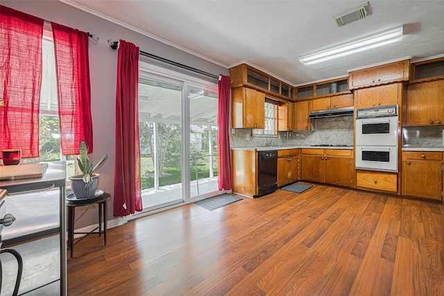 220 Palmyra St, Houston, TX 77022 - kitchen featuring under cabinet range hood, black appliances, light countertops, brown cabinetry, and wood finished floors