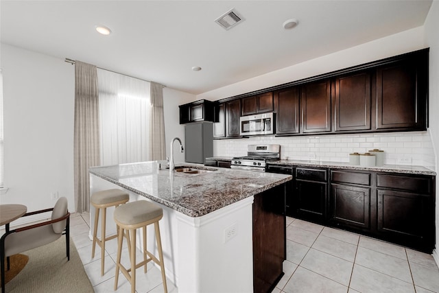 8310 Remington Bluff Ln, Richmond, TX 77407 - kitchen featuring stainless steel appliances, a sink, a kitchen bar, a kitchen island with sink, and light stone countertops