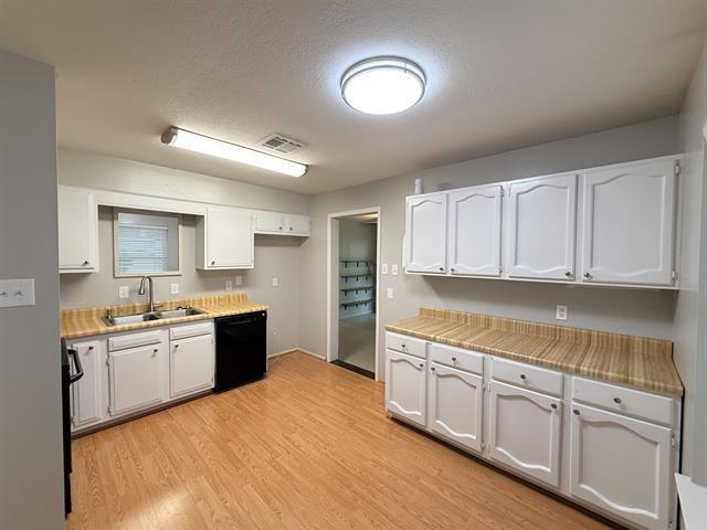 9410 Guy Cir, Beaumont, TX 77707 - kitchen with dishwasher, a sink, light wood-style flooring, white cabinets, and light countertops