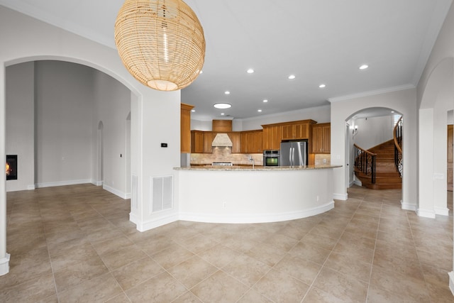 504 High Meadow Ranch Dr, Magnolia, TX 77355 - kitchen with stainless steel appliances, arched walkways, brown cabinetry, light stone counters, and recessed lighting