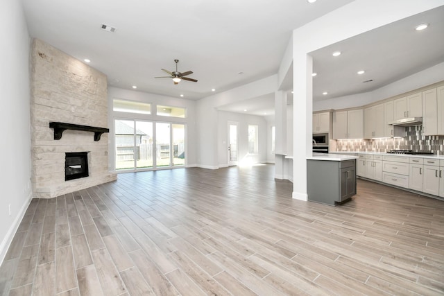 20922 Whirlaway Green Cir, Tomball, TX 77377 - unfurnished living room with a ceiling fan, recessed lighting, light wood-style floors, a stone fireplace, and baseboards
