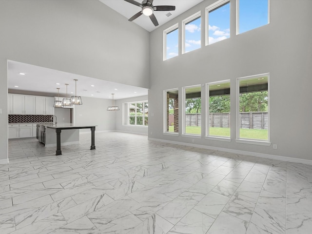 2107 Jitterbug Ln, Katy, TX 77493 - unfurnished living room featuring light marble finish flooring, a high ceiling, a ceiling fan, and baseboards