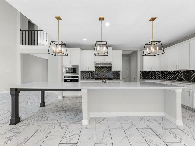 2107 Jitterbug Ln, Katy, TX 77493 - kitchen with stainless steel appliances, under cabinet range hood, light marble finish floors, light countertops, and recessed lighting